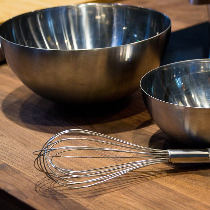 Beater for whipping in stainless steel and bowls on a wooden table.