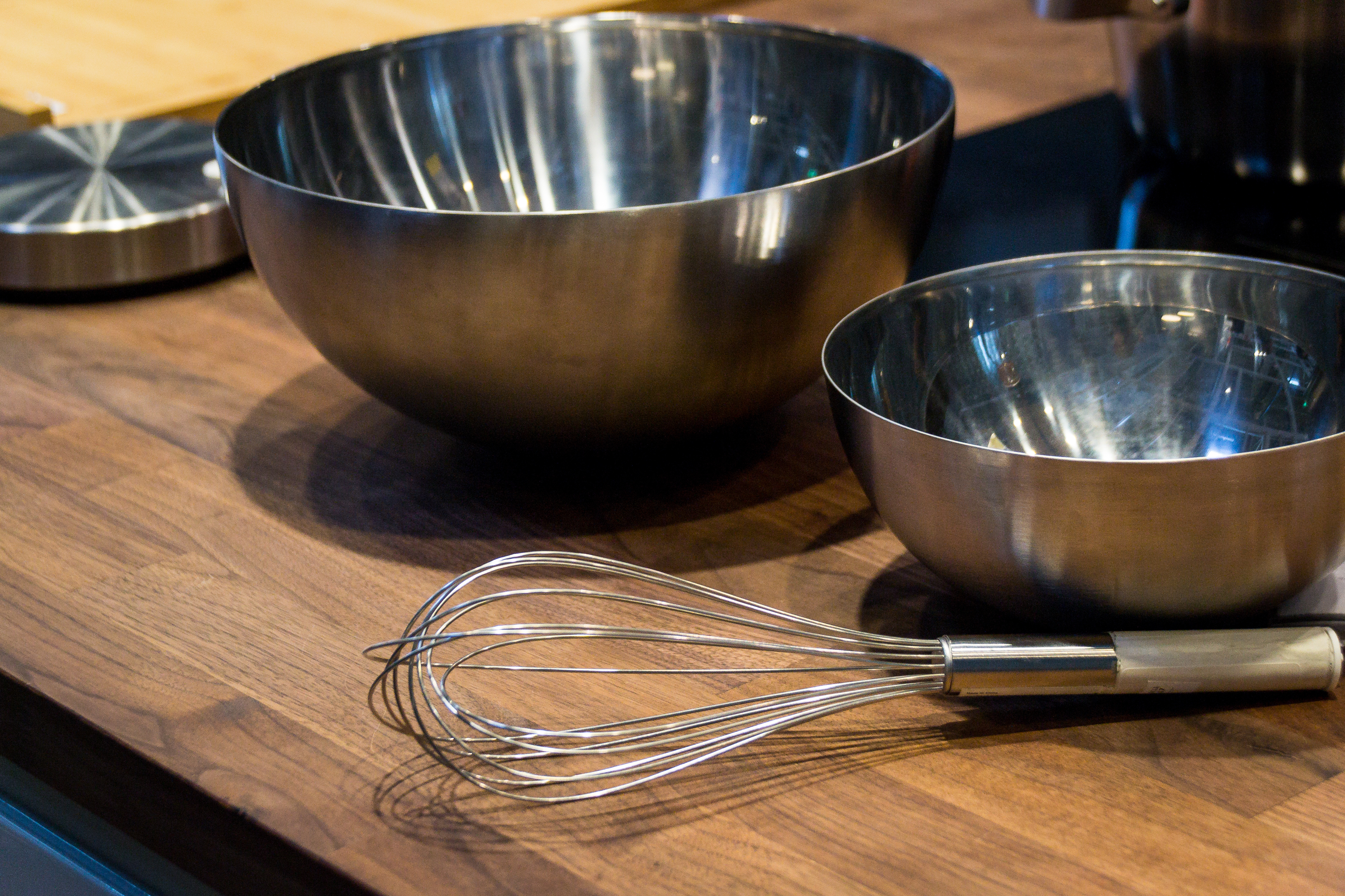 Beater for whipping in stainless steel and bowls on a wooden table.